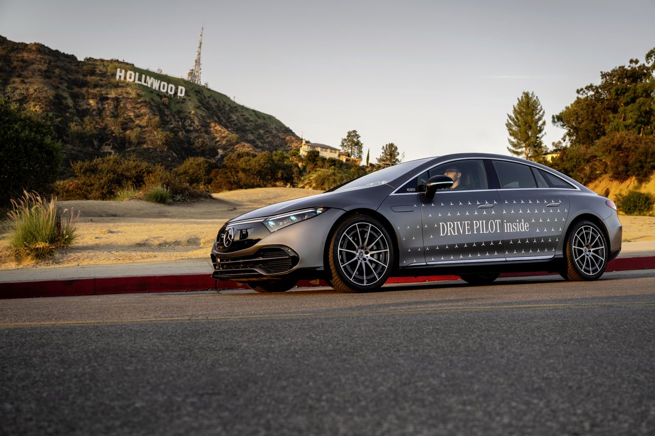 Gray Mercedes-Benz EQS DRIVE PILOT test car with turquoise marker lights on a Los Angeles street below the Hollywood sign