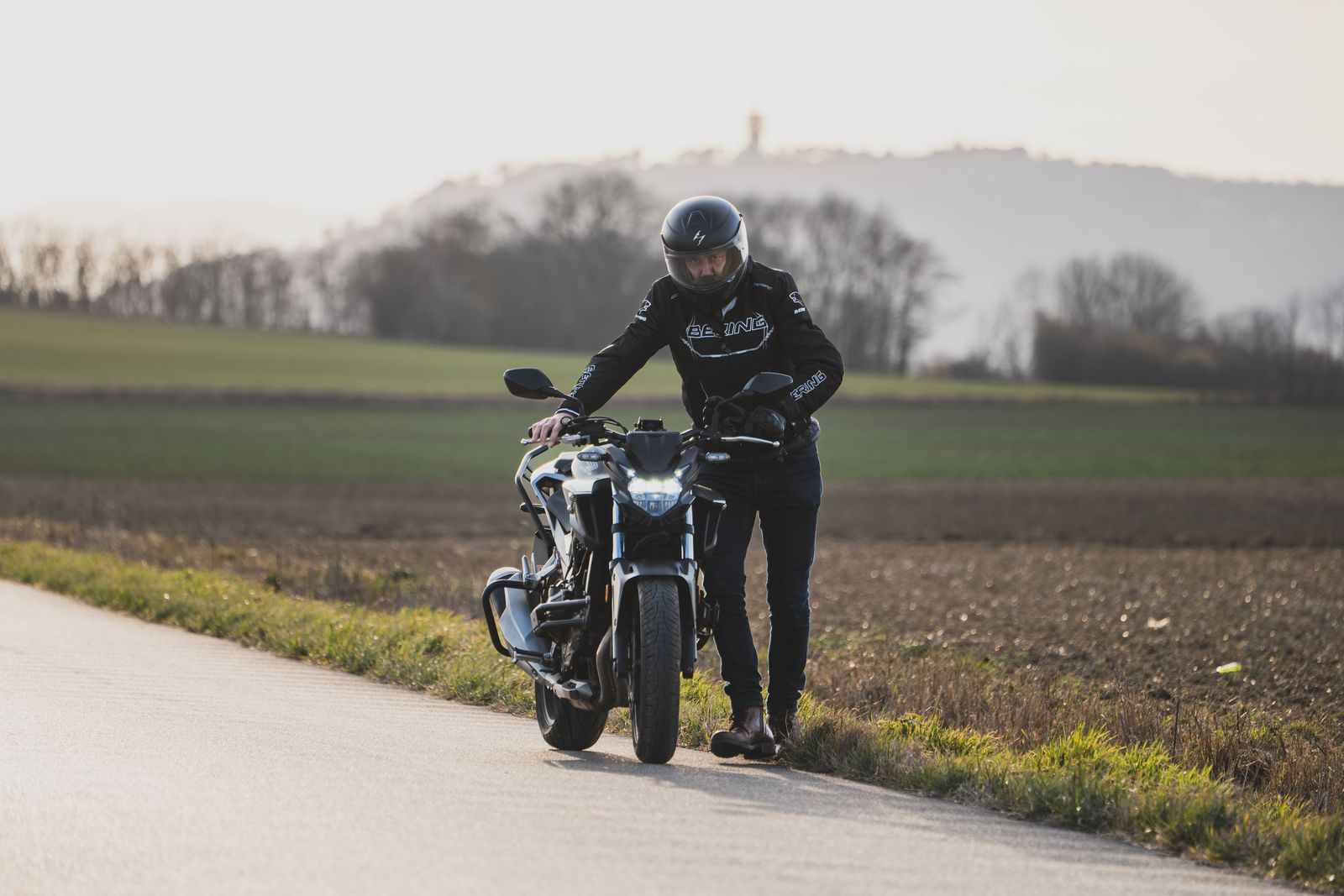 Motorcyclist in gear standing beside a motorcycle on a rural road