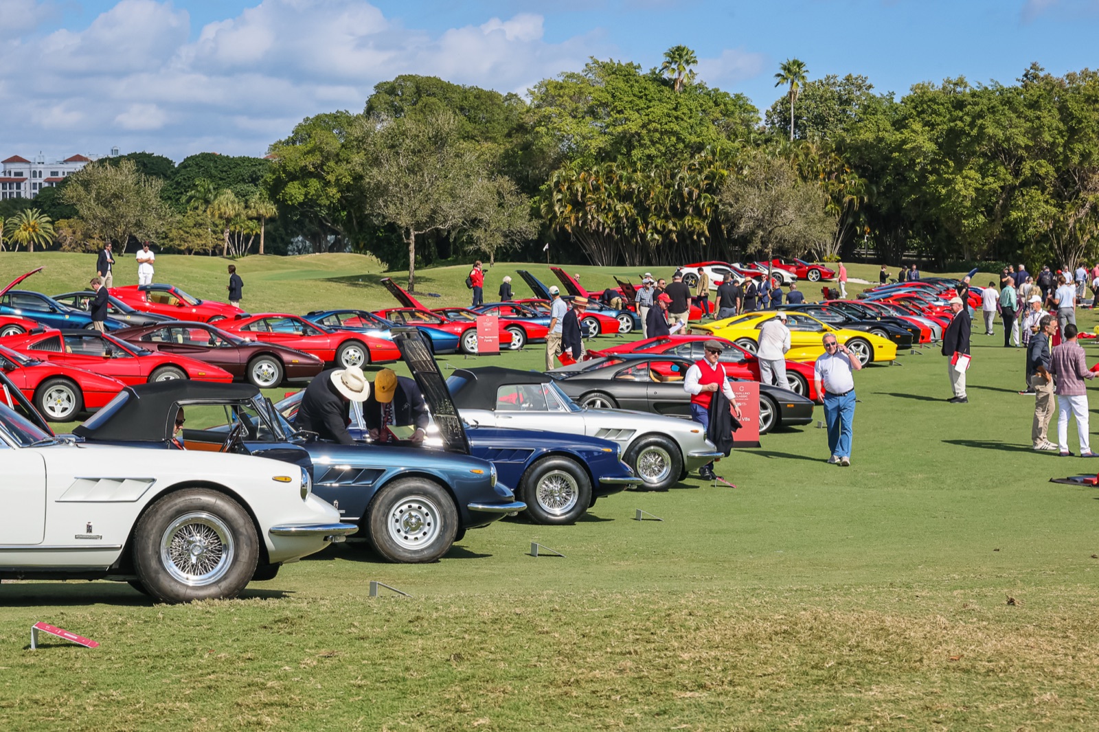 Visitors look under the hood of a blue 1960s Ferrari spider at the 2026 Palm Beach Cavallino Classic, with rows of red, yellow and black Ferraris behind