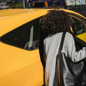 Passenger opening the rear door of a yellow car on a city street