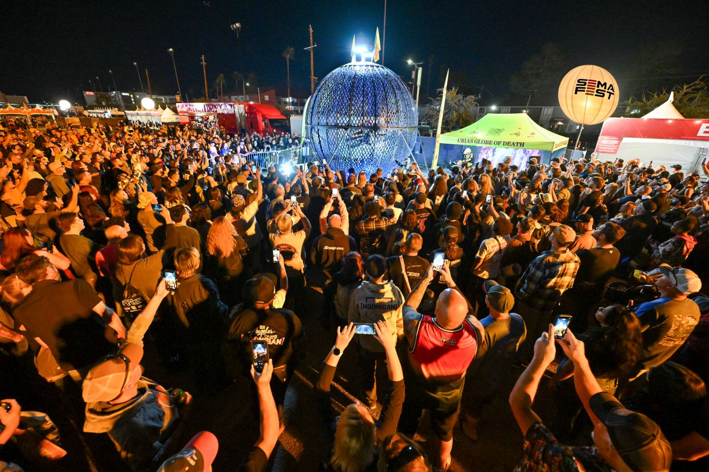 A crowd surrounds the steel Globe of Death sphere at SEMA Fest at night