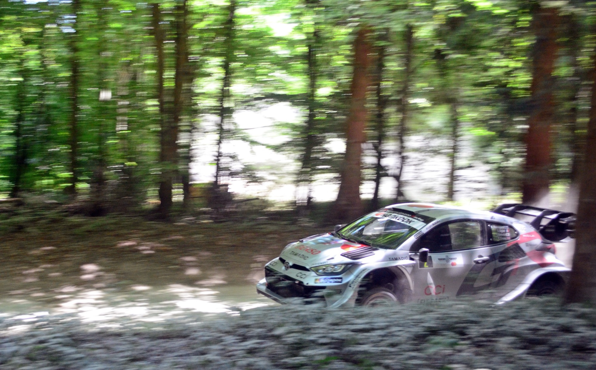 Silver and red Toyota GR Yaris Rally1 driving past trees on the forest rally stage at the 2025 Goodwood Festival of Speed