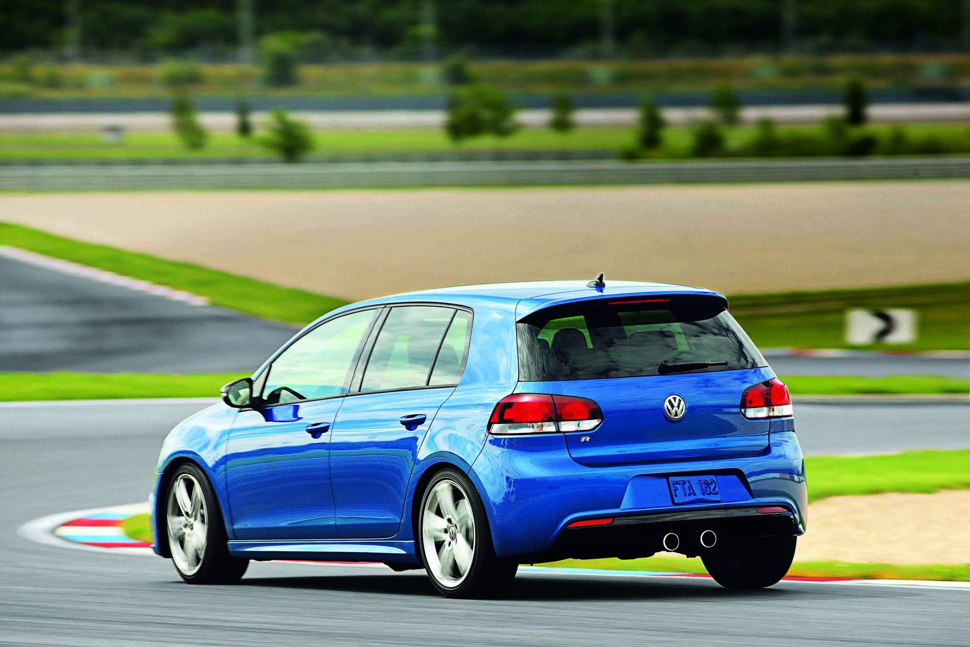 Rear three-quarter view of a blue four-door Volkswagen Golf R with center twin exhaust tips on a race track