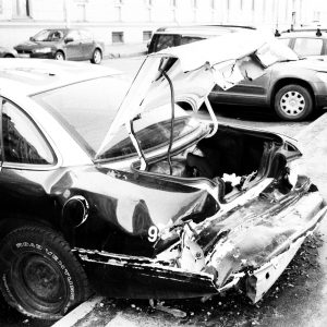 Black and white photo of a wrecked car parked on a city street